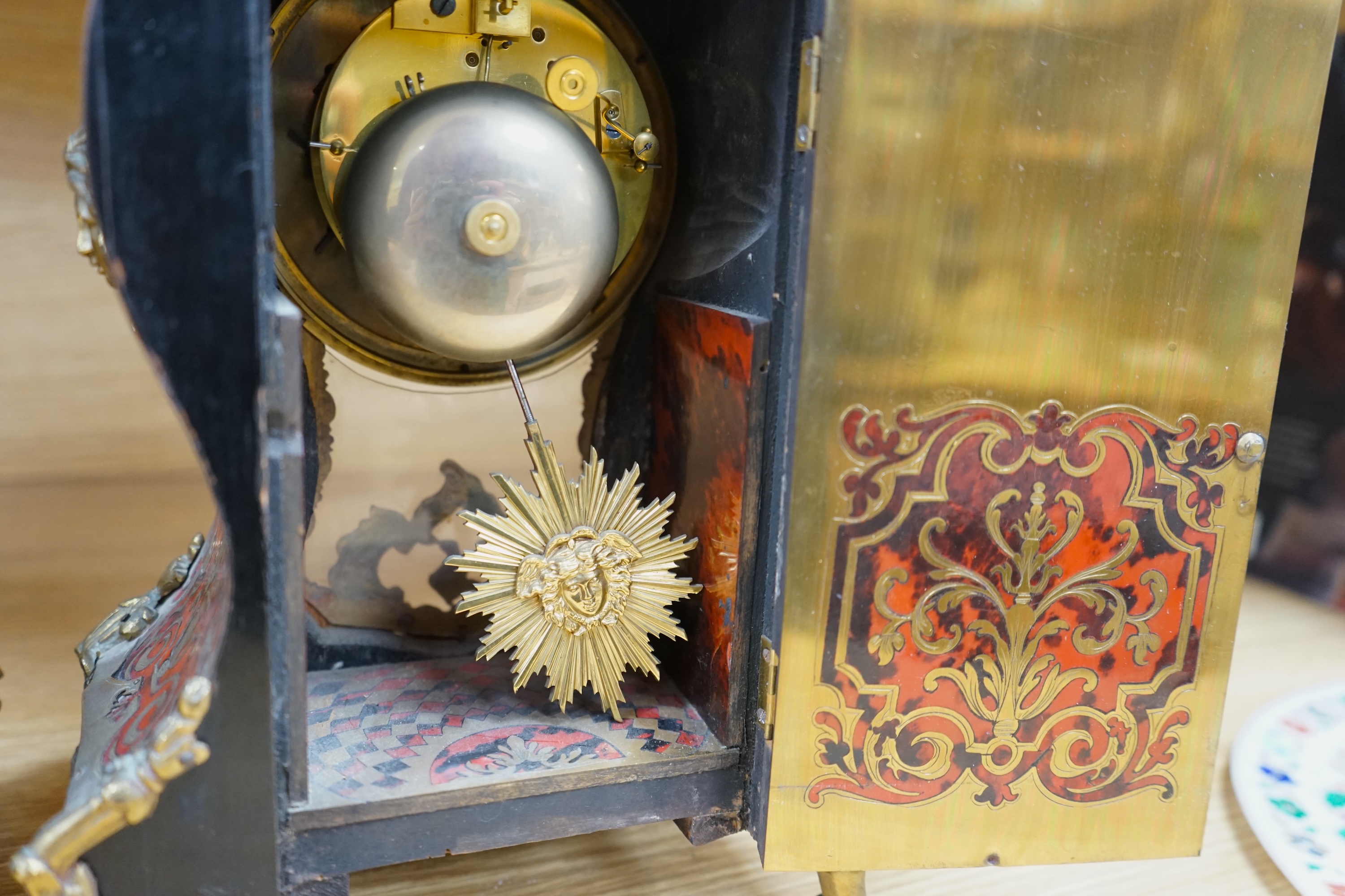 A French scarlet Boulle clock, and original bracket, the waisted case with glass front enclosing boulle interior and sunburst pendulum, c. 1860, clock 42cm high. Condition - fair, untested